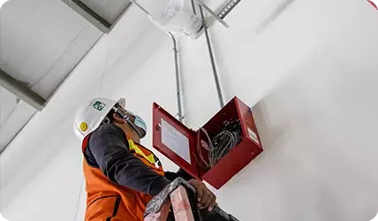 Ingeniero realizando mantenimiento preventivo a un sistema de alarma contra incendio, limpiando y revisando sensores y sus conexiones para asegurar su correcto funcionamiento.